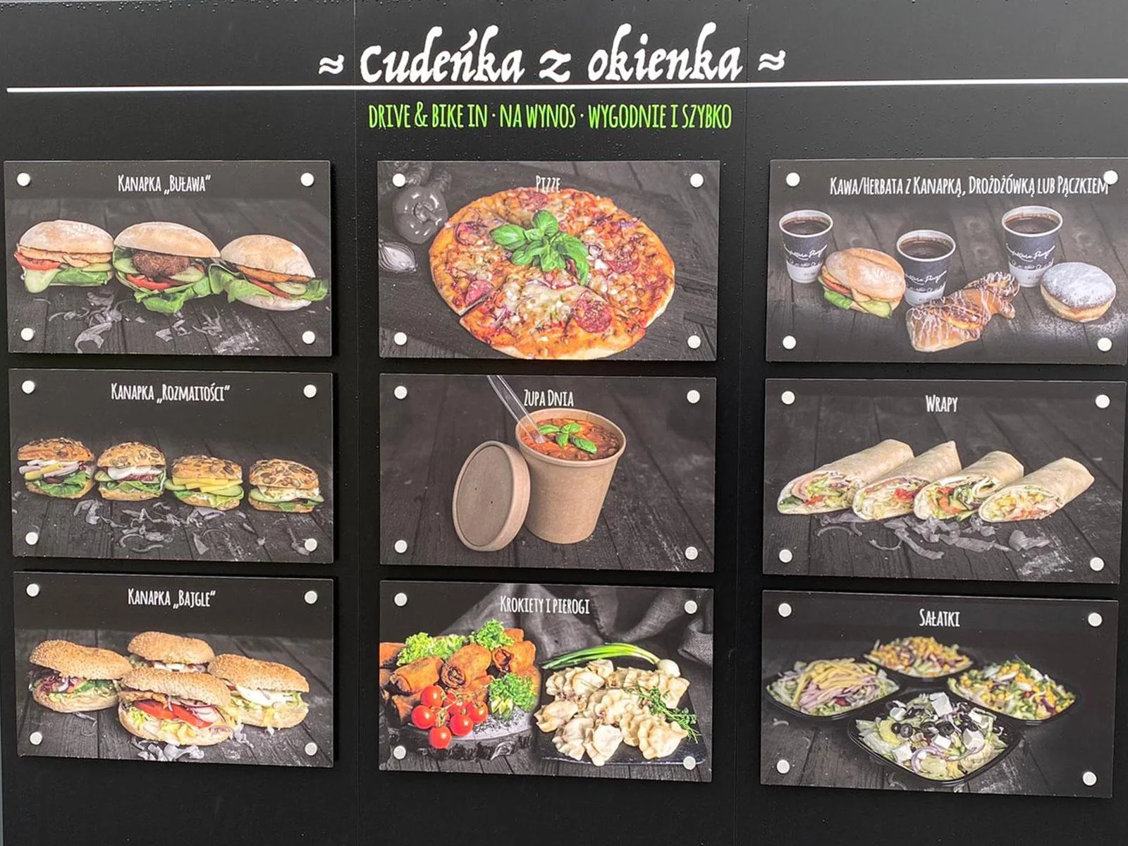 Tablica oferty przy okienku: kanapki, pizza, zapiekanki, kawa, sałatki i zestawy lunchowe
